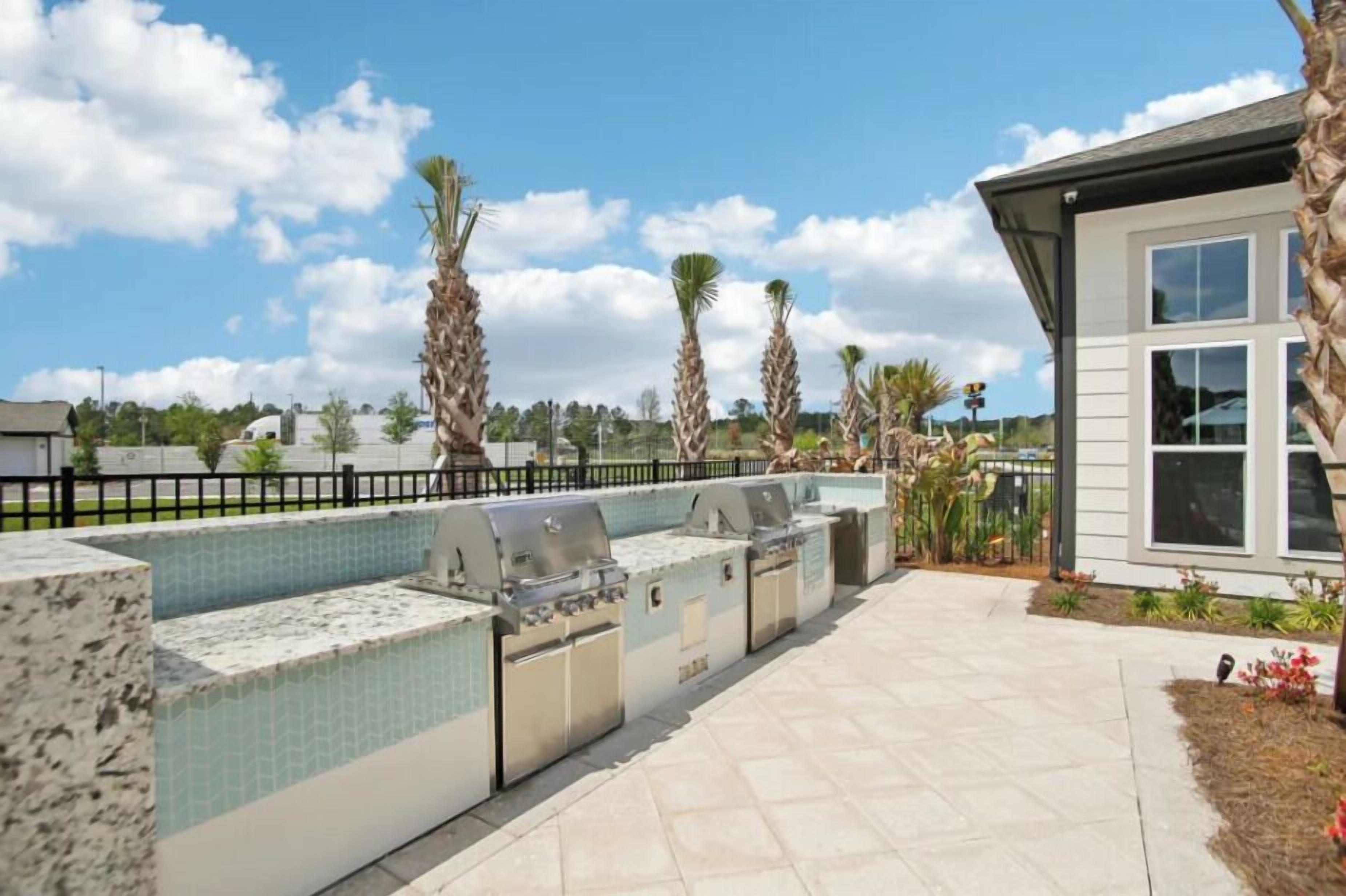 An outdoor patio with a built-in grill and seating area, surrounded by palm trees and a clear sky.