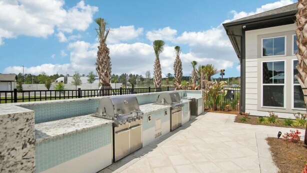Une terrasse extérieure dotée d’un barbecue intégré et d’un espace salon, entourée de palmiers et offrant une vue sur un ciel dégagé.
