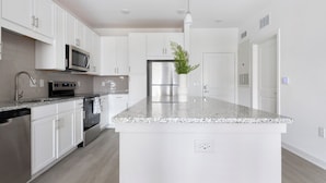 A modern kitchen with white cabinetry, stainless steel appliances, a granite countertop, and a central island. - Landing Apartments near JAX (Jacksonville)