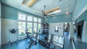 A spacious gym with exercise equipment, large windows, and a ceiling fan. - Landing Apartments near JAX (Jacksonville)