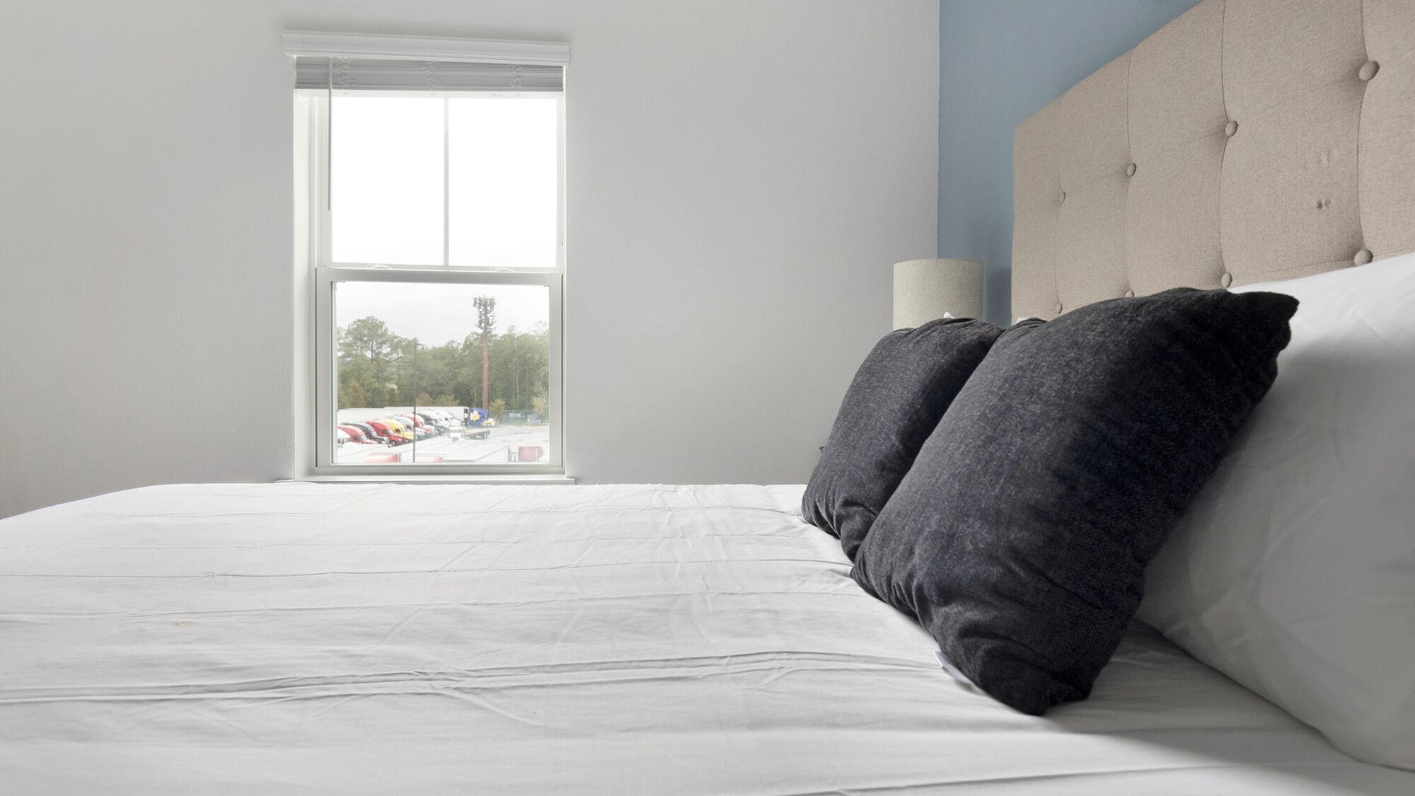 A bedroom with a large bed, a window with a view of parked trucks, and a tufted headboard.
