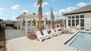 A poolside area with sun loungers, a covered seating area, and a building with large windows. - Landing Apartments near JAX (Jacksonville)