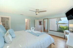Une chambre à coucher avec un lit, un ventilateur de plafond, une télévision et une vue sur l’extérieur.