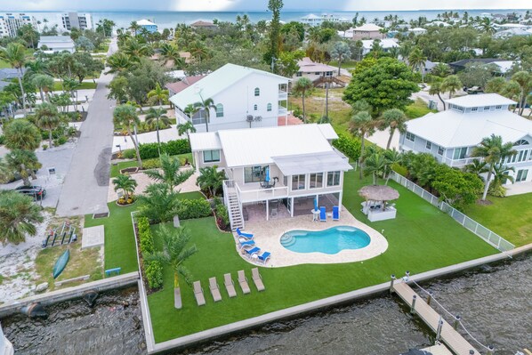 Une grande maison avec une piscine, entourée d’une pelouse bien entretenue et de palmiers.