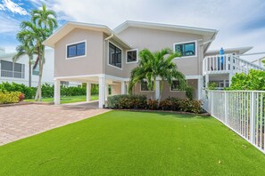 Une maison à deux étages avec un patio couvert, une pelouse bien entretenue et une clôture blanche.