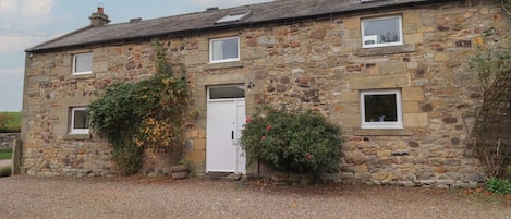 A stone house with a gravel driveway, a white door, and small windows.