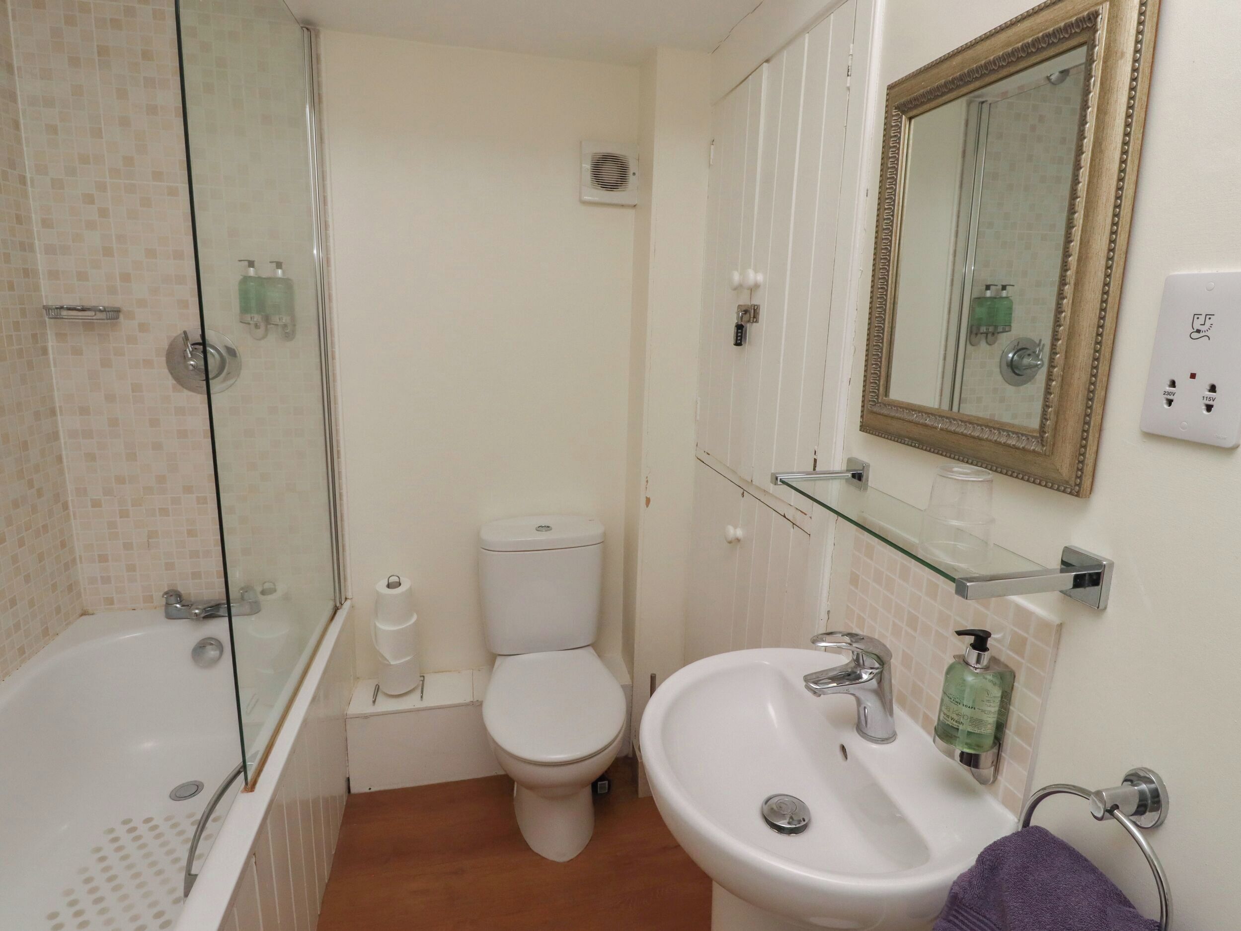 A bathroom with a glass-enclosed shower, a toilet, a sink, and a mirror with a decorative frame.