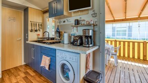 A compact kitchen with a washing machine, a coffee machine, and a flat-screen TV. - Mobile Home 'Location Agde' with Private Terrace, Wi-Fi and Air Conditioning (Agde)