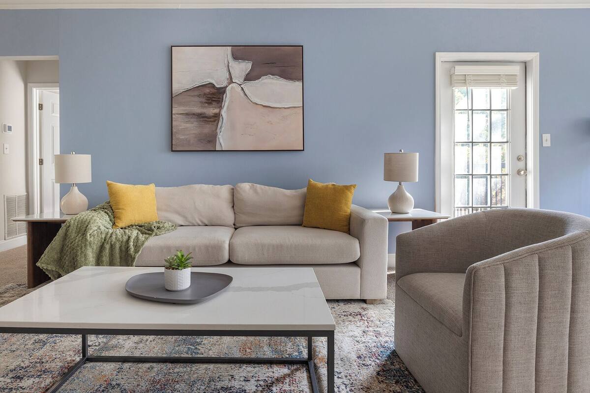 A living room with a beige sofa, a grey armchair, a coffee table, and a painting on the wall.