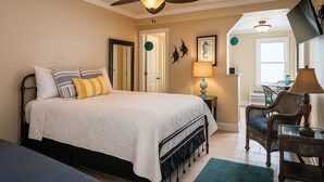 Ein Schlafzimmer mit einem Bett, einem Deckenventilator, einem Nachttisch, einer Lampe, einem Sessel und einem Fenster.