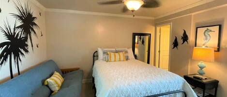A bedroom with a bed, a sofa, a ceiling fan, a nightstand, and wall decorations.