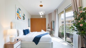A modern bedroom with a large bed, bedside tables, a ceiling light fixture, and a view of the outside balcony.