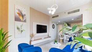 A modern living room with a TV, blue sofas, and a dining area.