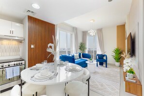 Une cuisine moderne avec des meubles blancs, une cuisinière en acier inoxydable et un coin repas agrémenté d’une table ronde pour quatre personnes.