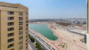 A high-rise building with multiple balconies overlooking a coastal area with a beach and a road with vehicles.