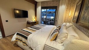 Habitación de hotel con una cama grande, un televisor de pantalla plana en la pared, una mesita de noche y vistas al exterior a través de un ventanal.