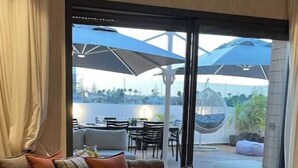 Una sala de estar moderna con un sofá, una mesa de centro redonda y vistas a un patio exterior con sombrillas y asientos.