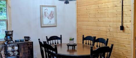 A wooden-paneled room with a round table and chairs, a chandelier, and a coffee station.