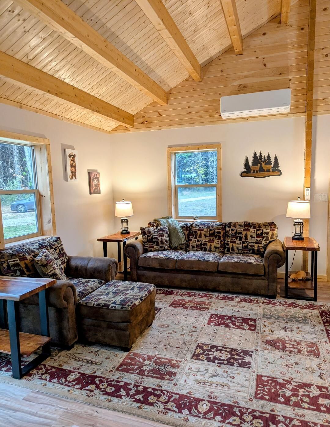 A cozy living room with wooden beams, a patterned sofa, a rug, and a view of the outdoors.