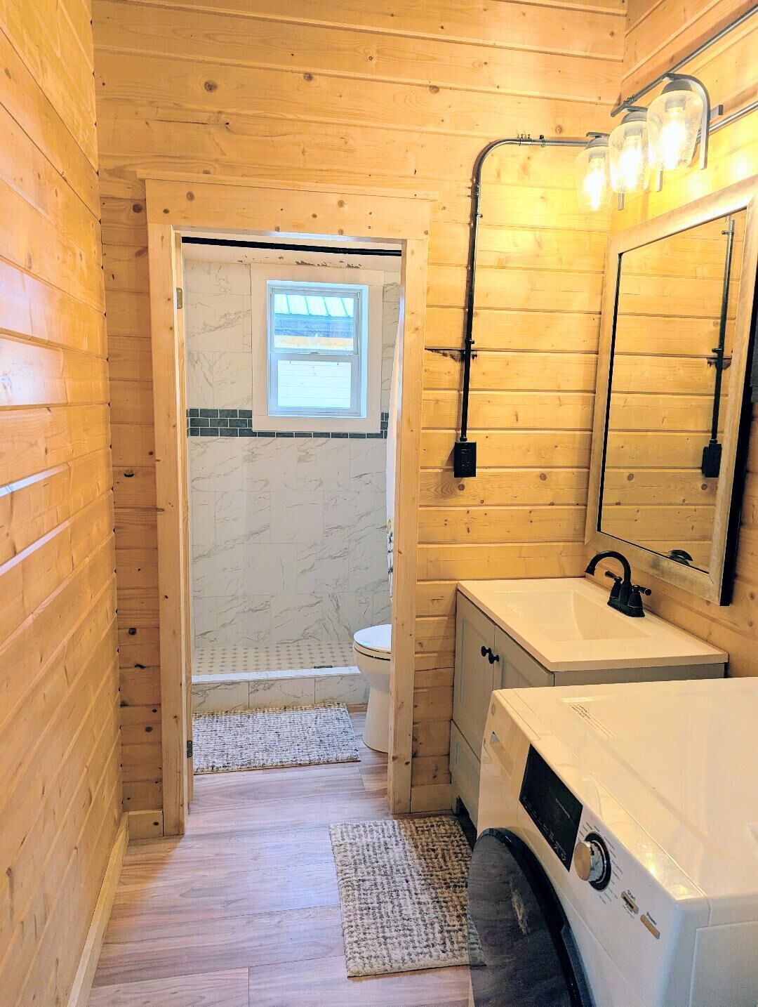 Pieni, puinen mökkikylpyhuone, jossa on wc, pesuallas ja pesukone.