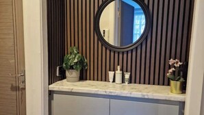 Un baño con pared de listones de madera, un espejo redondo, encimera de mármol y un armario.