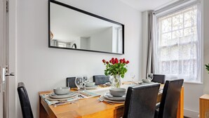 Un comedor con una mesa de madera dispuesta para seis comensales, un florero con flores rojas y un espejo grande sobre la mesa.