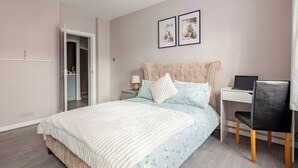 Un dormitorio con cama, escritorio, silla y puerta que da a un baño.
