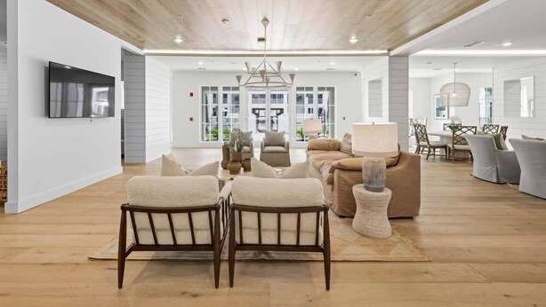A spacious living area with a wooden ceiling, a large sofa, a coffee table, and a TV mounted on the wall. - Landing Apartments Downtown Palm Coast (Palm Coast)
