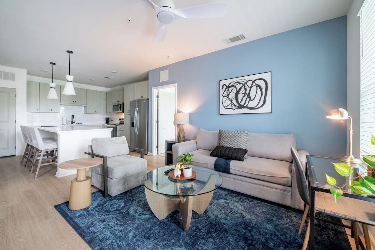 A modern living room with a glass coffee table, a grey sofa, and a dining area with a table and chairs.