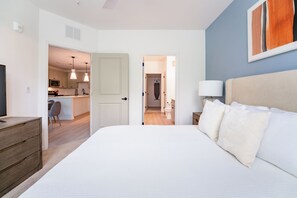A bedroom with a large bed, a bedside table, a lamp, and a painting on the wall. - Landing Apartments Downtown Palm Coast (Palm Coast)