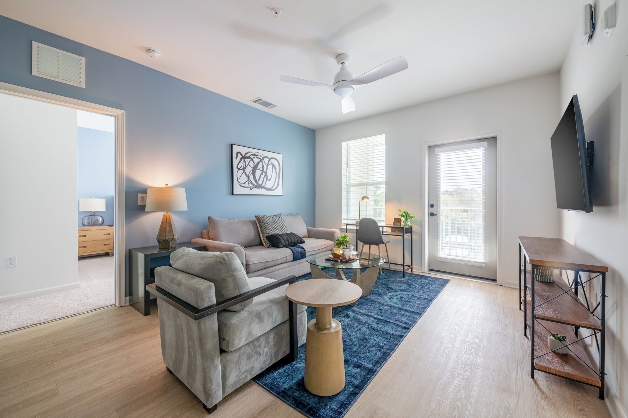 A modern living room with a blue accent wall, a ceiling fan, a flat-screen TV, and a dining area with a table and chairs.
