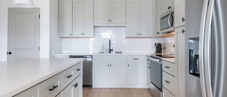 A modern kitchen with white cabinetry, a stainless steel refrigerator, and a dishwasher.