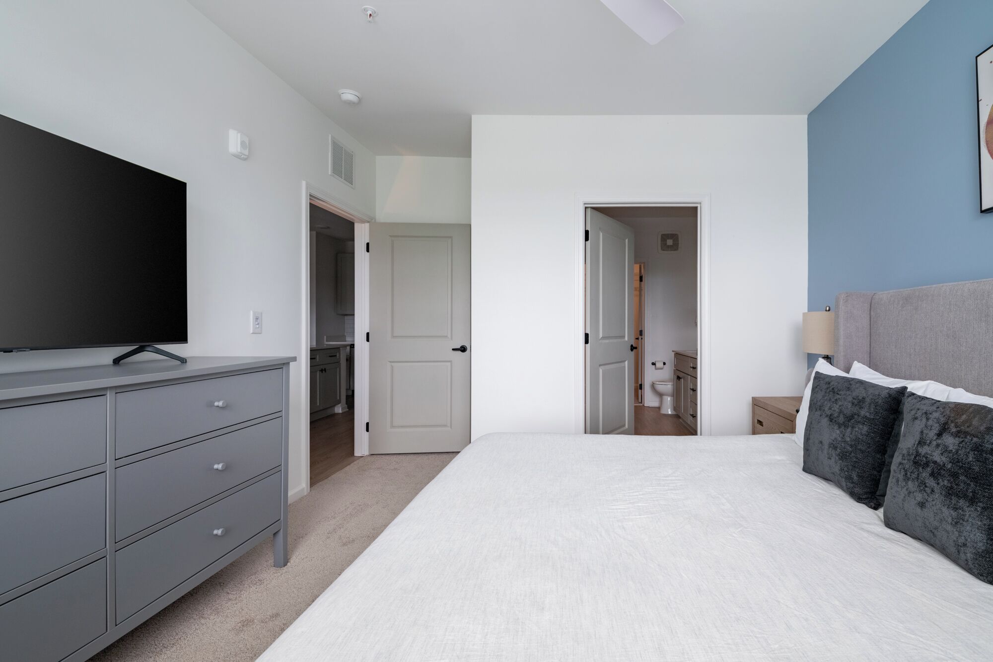 Ein Schlafzimmer mit einem Bett, einem Fernseher auf einer Kommode und einer Tür zu einem Badezimmer.