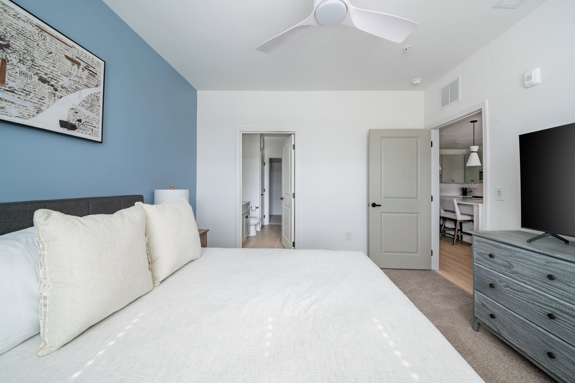 A bedroom with a bed, a dresser, a ceiling fan, and a TV.