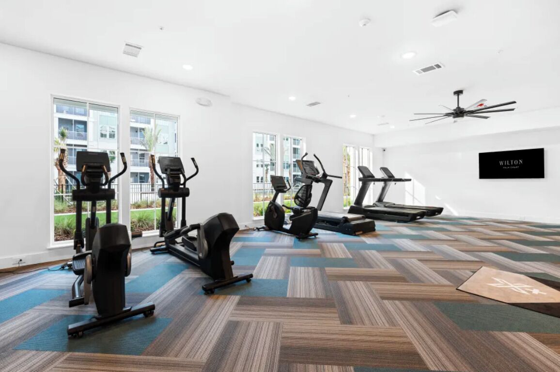 A gym with treadmills, elliptical machines, and a ceiling fan.