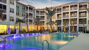 A hotel with a swimming pool, multiple balconies, and palm trees. - Landing Apartments Downtown Palm Coast (Palm Coast)
