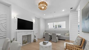 A modern living room with a fireplace, a flat-screen TV mounted above it, and a dining area with a table and chairs. - Landing Apartments Downtown Palm Coast (Palm Coast)