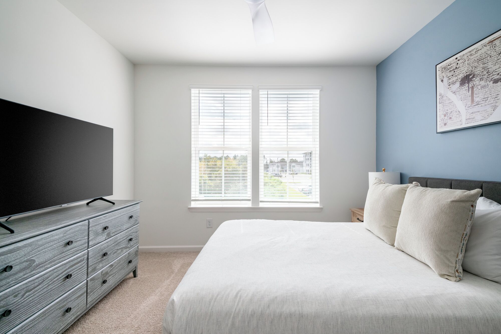 A bedroom with a bed, a dresser, a TV, and a window with blinds.