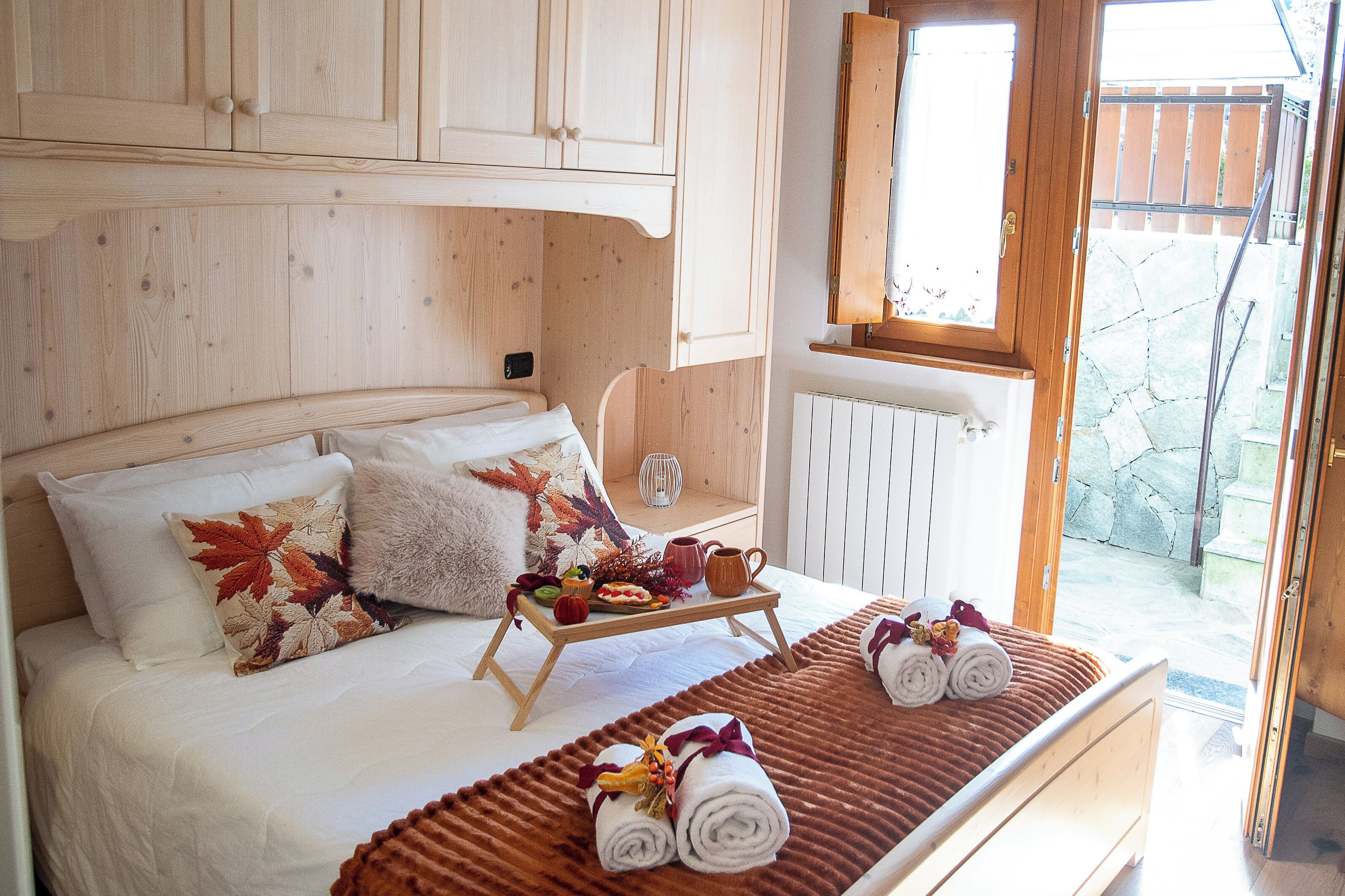Un dormitorio acogedor con cama, almohadas, una bandeja con desayuno y vistas al exterior.