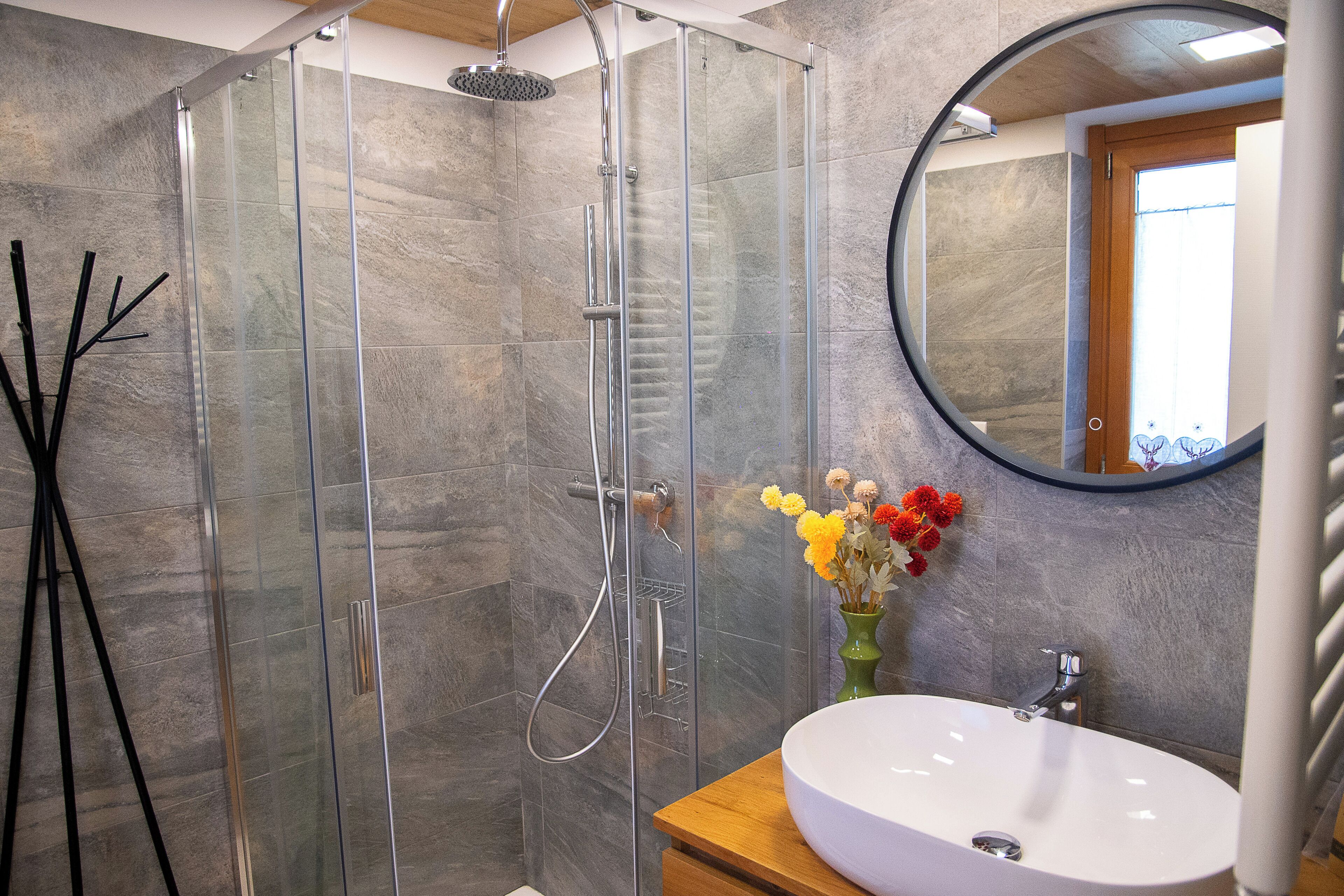 A modern bathroom with a glass-enclosed shower, a wooden vanity, and a round mirror.