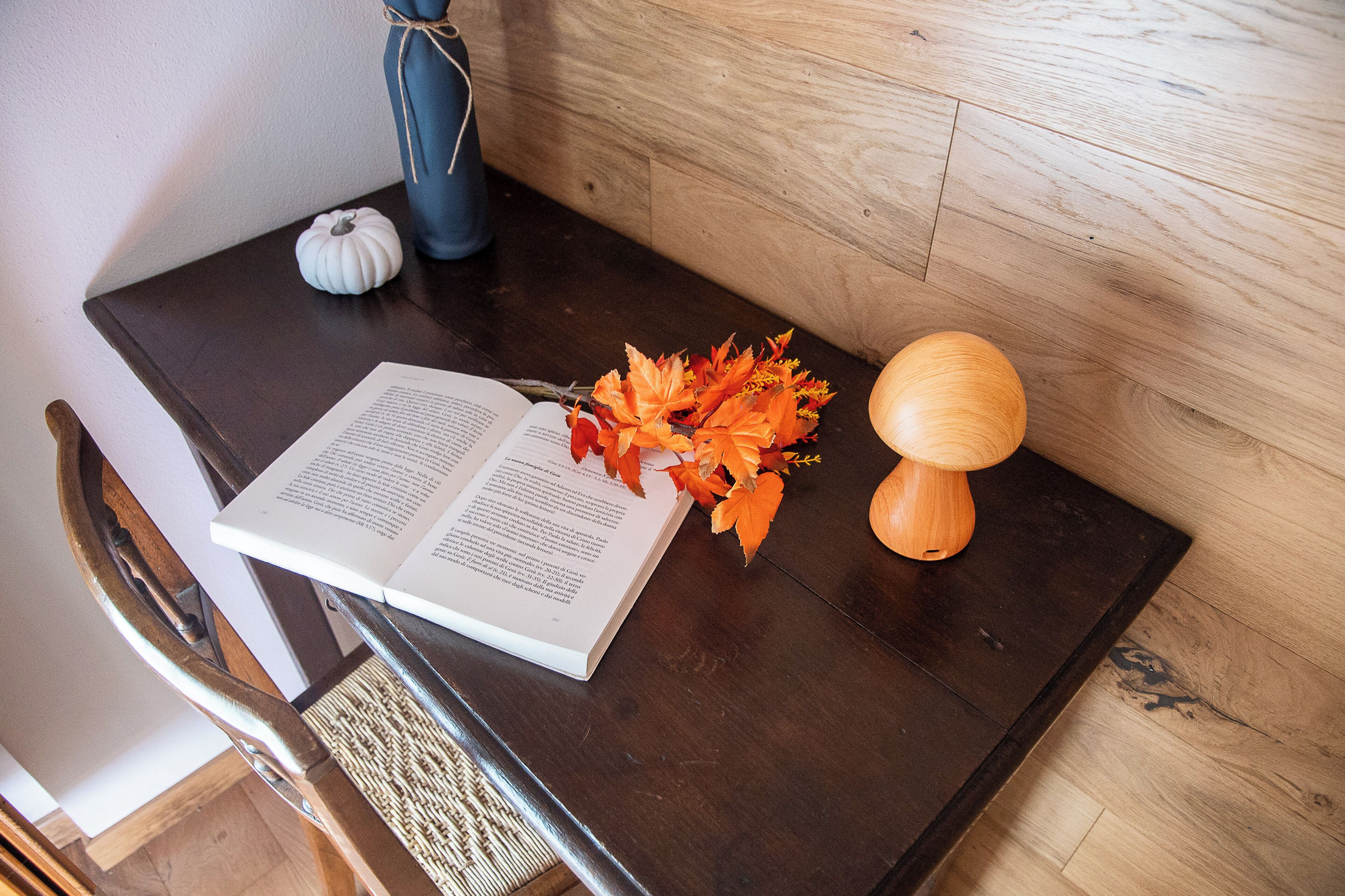 A wooden table with a book, a small white pumpkin, and autumn leaves.