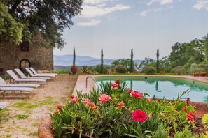 Ein Poolbereich mit Liegestühlen, einem Blumenbeet und einem Steinhaus im Hintergrund.