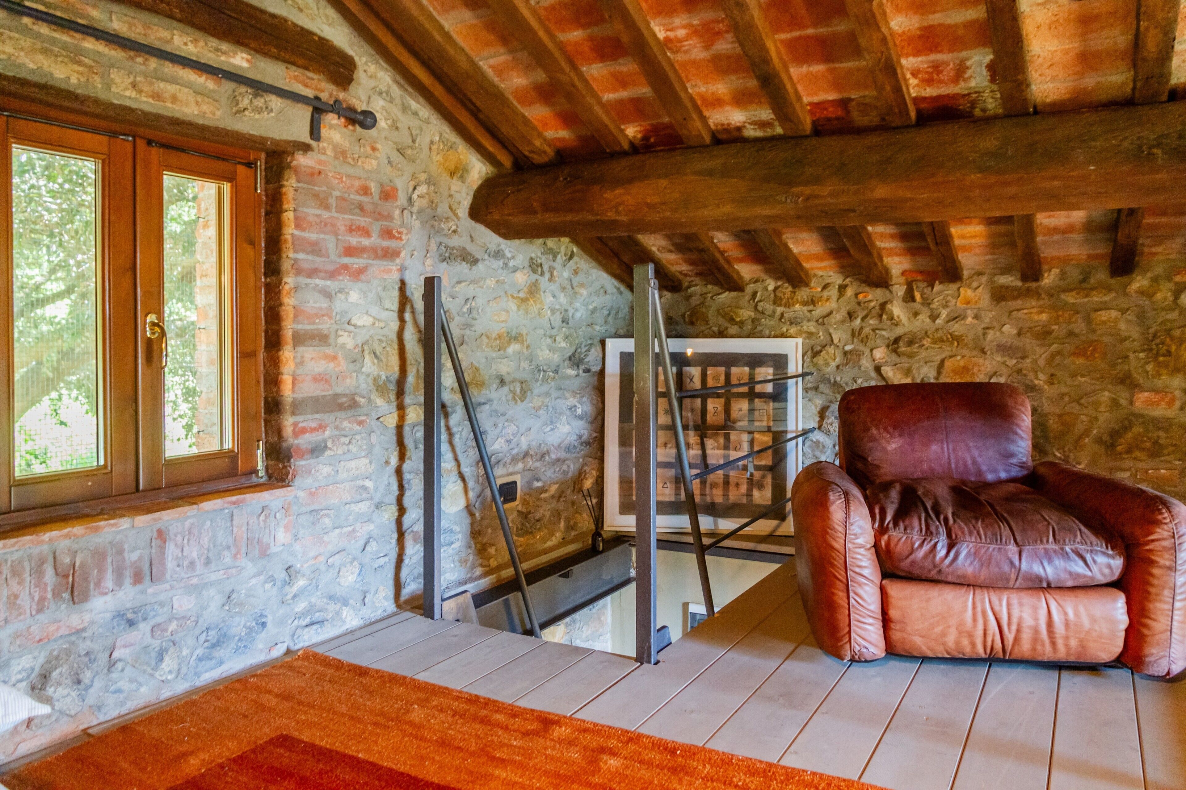 A rustic room with a stone wall, wooden beams, a leather chair, and a window with a view.