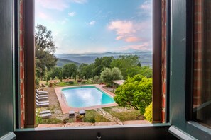 A view through a window of a swimming pool surrounded by greenery and a mountainous landscape. - 'Ficaiola' Room with Shared Pool and Garden (Massa Marittima)