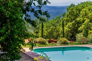 Une piscine entourée d’une végétation luxuriante, avec une vue sur les montagnes lointaines.