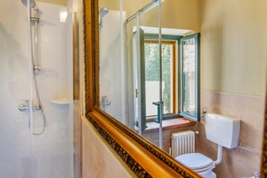 Une salle de bain avec douche, toilettes et une fenêtre donnant sur un espace verdoyant.