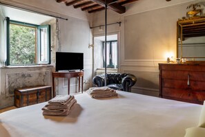 Una habitación con cama, televisor, cómoda, ventana y una silla.