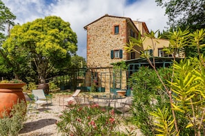 A stone building with a garden patio, outdoor seating, and a large tree.