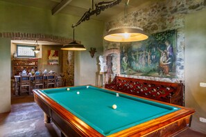 Une table de billard recouverte d’un drap vert, un banc en bois doté d’un dossier décoratif et une fresque murale.