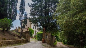 A gravel path leading to a building with a stone gate, surrounded by trees and greenery. - 'Corbellino' Room with Shared Pool and Garden (Massa Marittima)